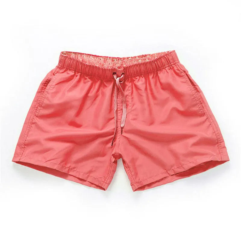 Men's plus size polyester surf shorts on a beach, showing straight leg fit in black and emerald green colours.