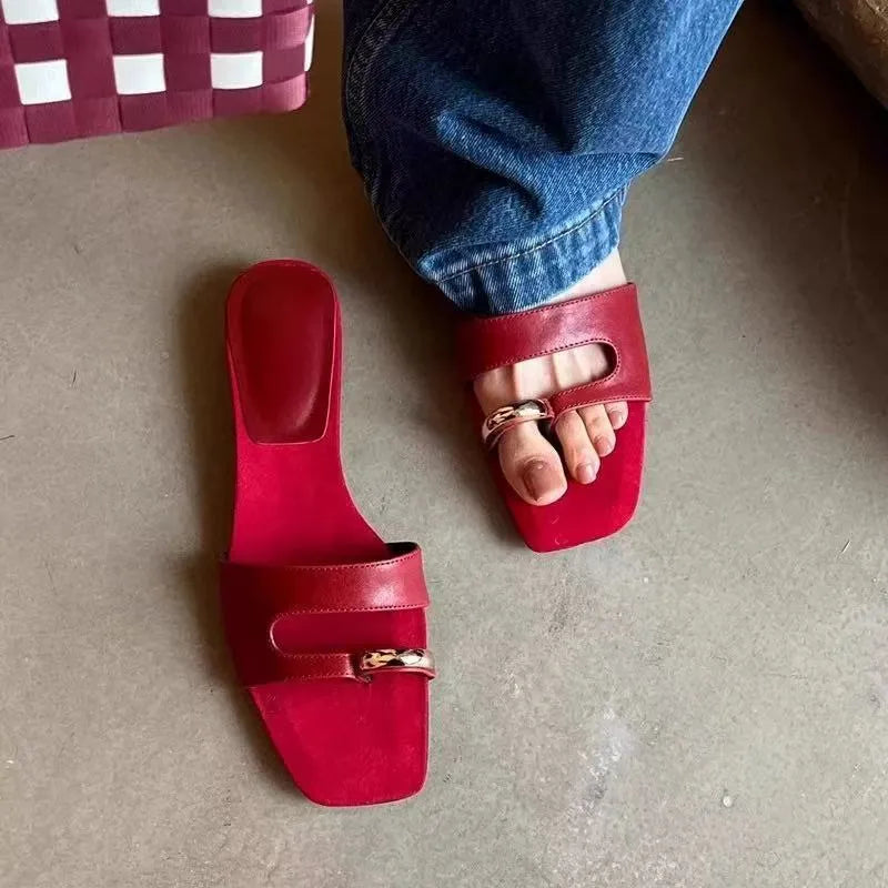 A pair of black square-toe slippers with a leather upper and light rubber sole on a wooden floor.