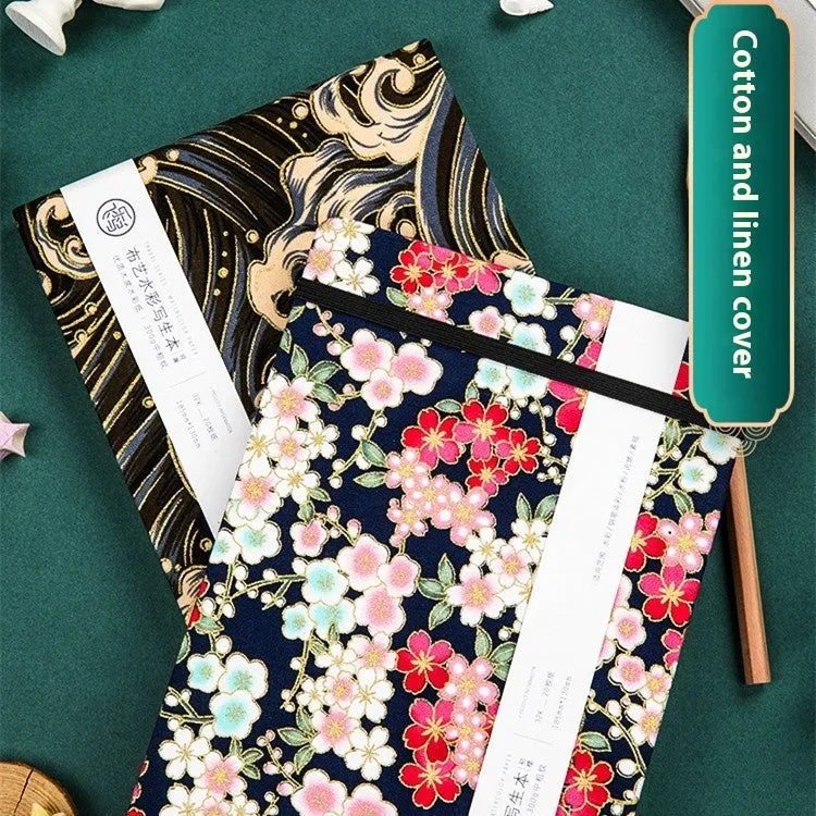 Feiluniao fabric cover watercolour notebook open on a table with brushes, 185mm length