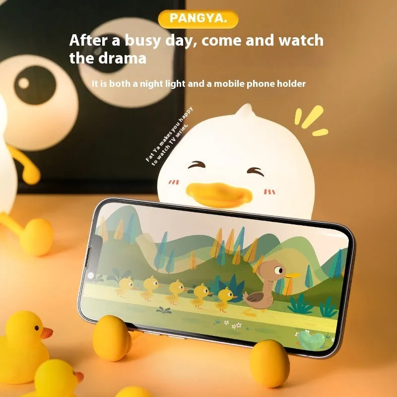 Chubby silicone night light lamp with phone holder on desk, showing soft LED glow and compact 108x104x128mm dimensions