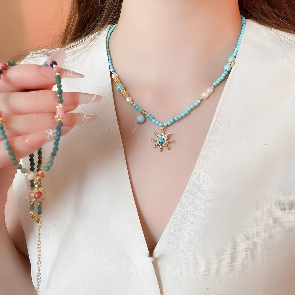 Stone sun pendant freshwater pearl necklace with gold blue pink chain on display.