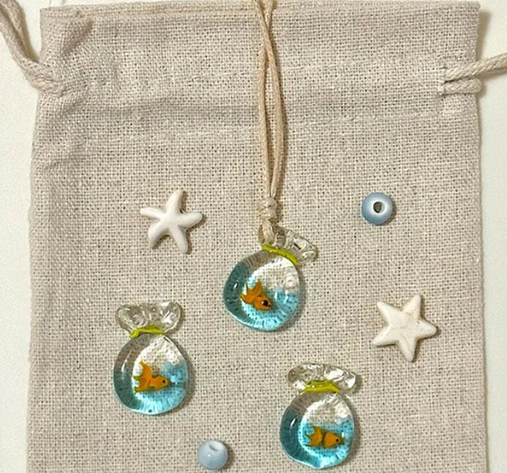 Women's necklace with small coloured glaze fish lucky bag pendant on a braided cotton and linen chain.