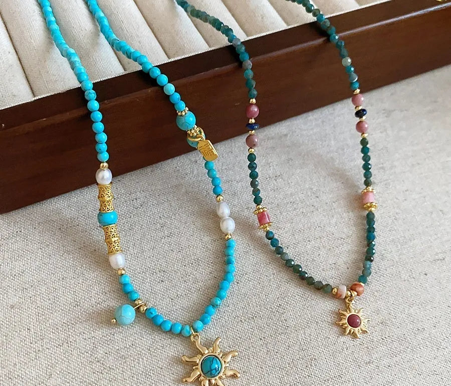 Stone sun pendant freshwater pearl necklace with gold blue pink chain on display.