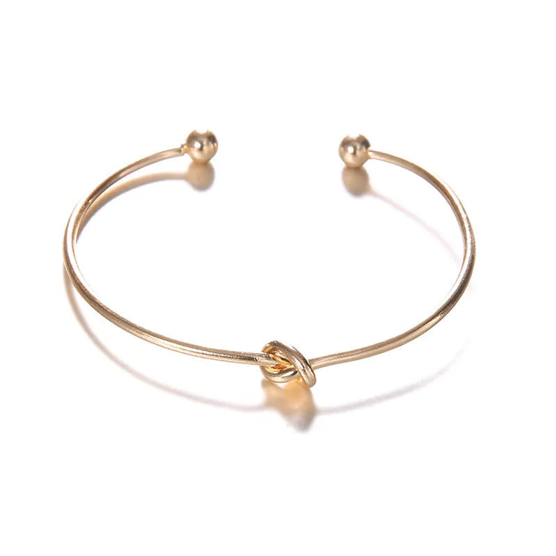 Gold electroplated alloy women's vintage cuff bracelet with knotted arrow design on a white background.