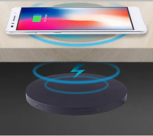 Black 75mm round wireless charging disc for embedding into desks, compatible with iPhone and Samsung phones.
