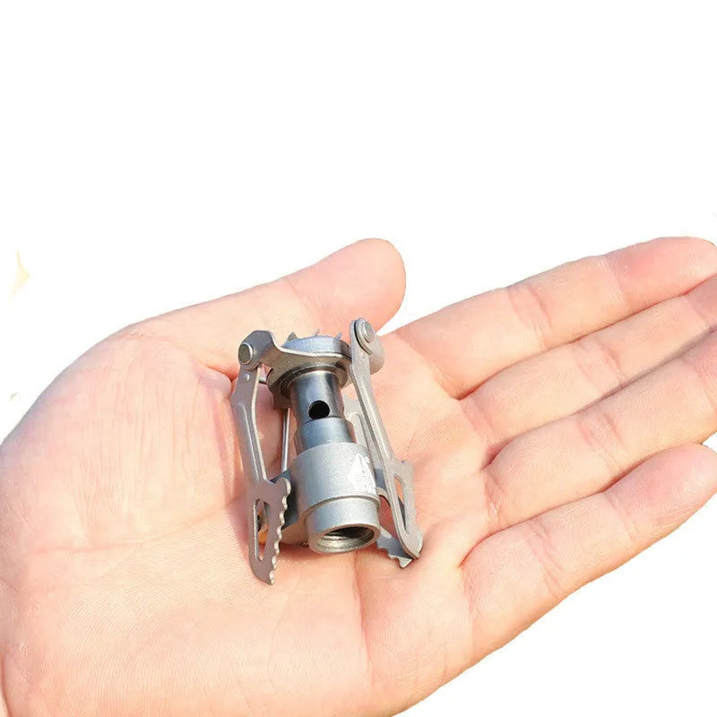 Portable metal camping gas stove with a one-piece burner, shown on a flat surface.