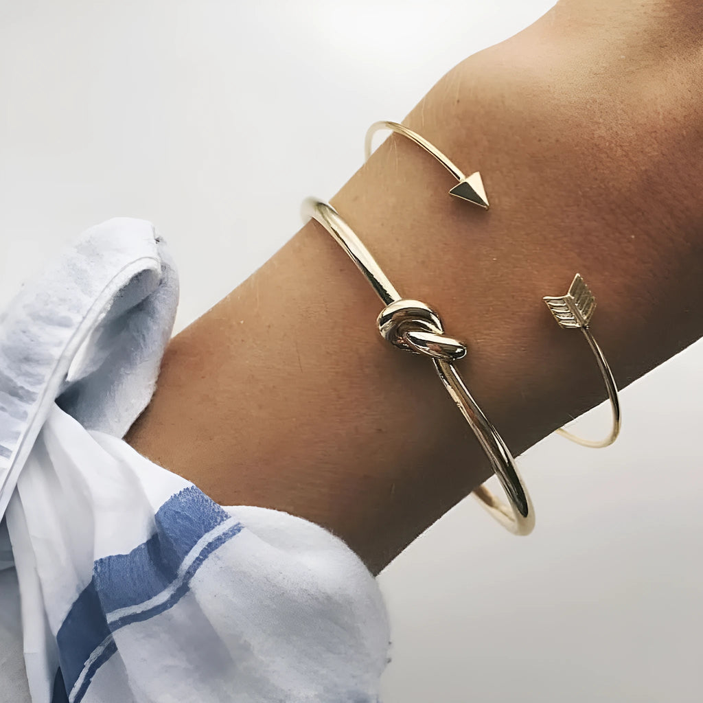 Gold electroplated alloy women's vintage cuff bracelet with knotted arrow design on a white background.