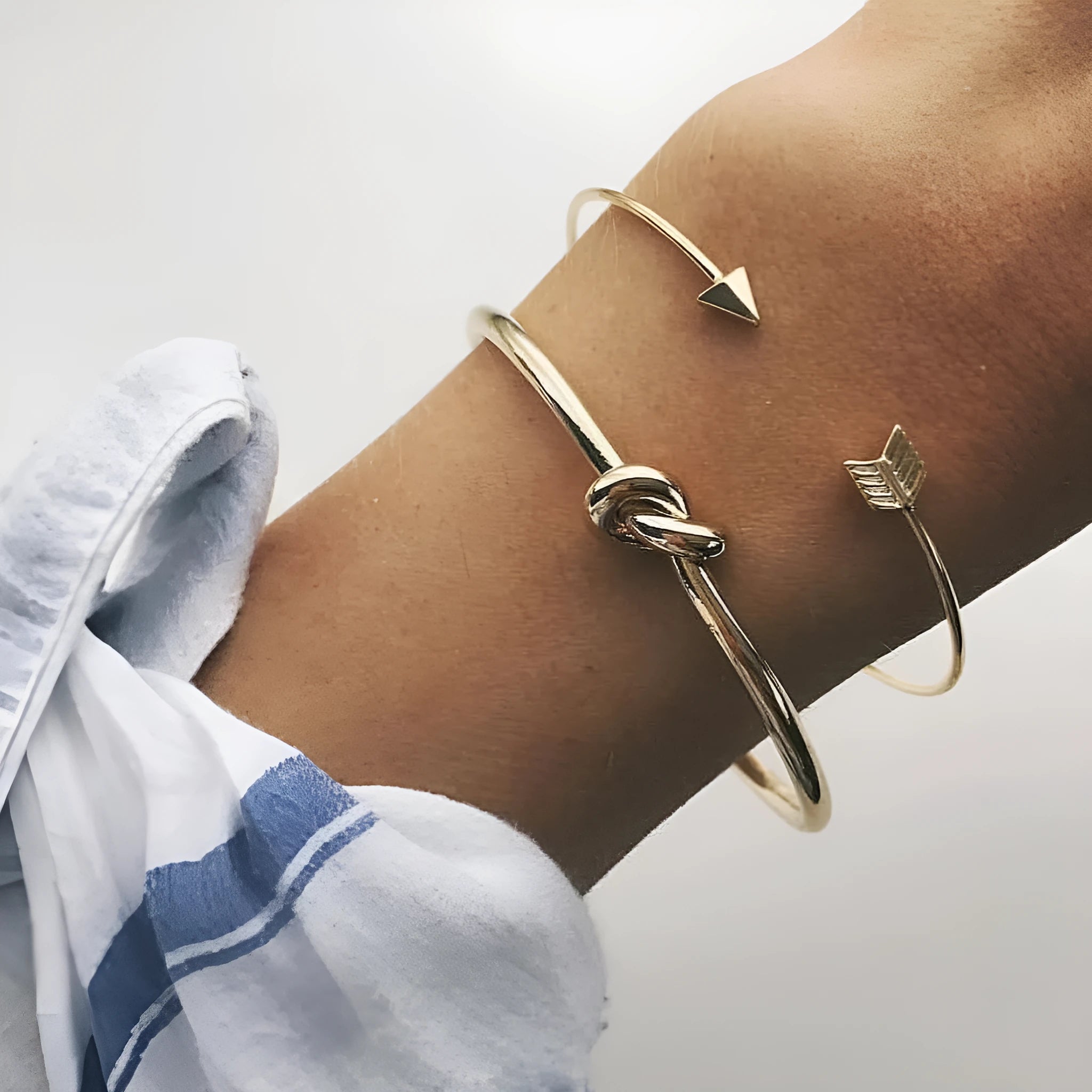 Gold electroplated alloy women's vintage cuff bracelet with knotted arrow design on a white background.