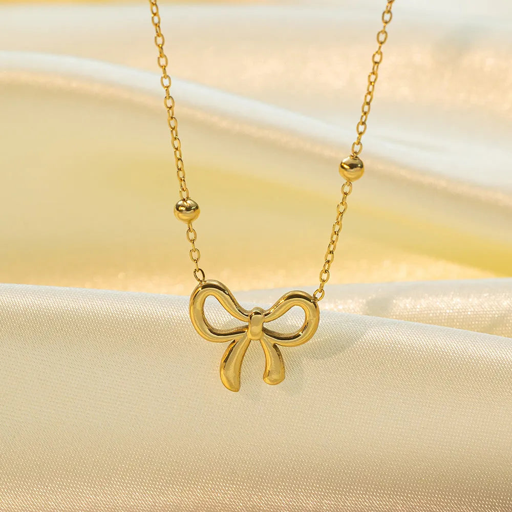 Gold titanium steel bow necklace on a cross chain, adjustable between 41cm and 50cm.
