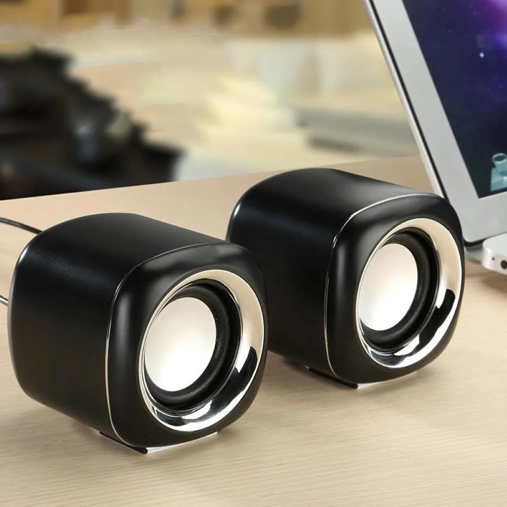 A pair of small black wired desktop computer speakers with a volume scroll wheel.