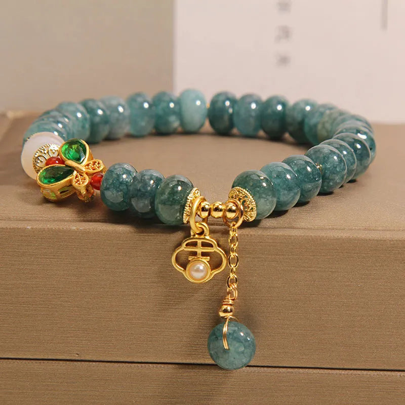 Close-up of a women's bracelet with blue water jade abacus beads, white agate, alloy inlay, and a butterfly clasp.