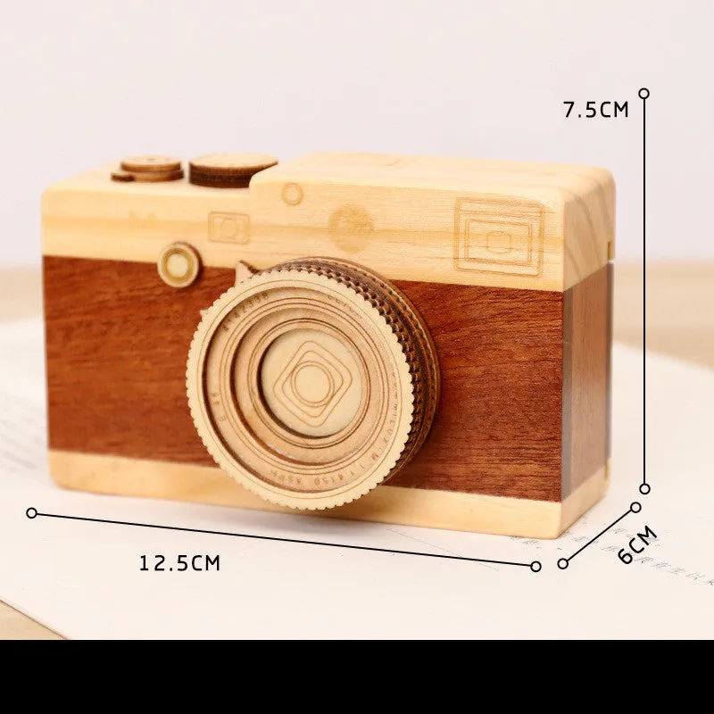 Wooden camera-shaped music box on a rotating stand, packaged in a carton box.