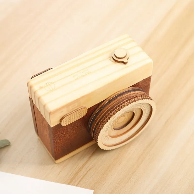 Wooden camera-shaped music box on a rotating stand, packaged in a carton box.