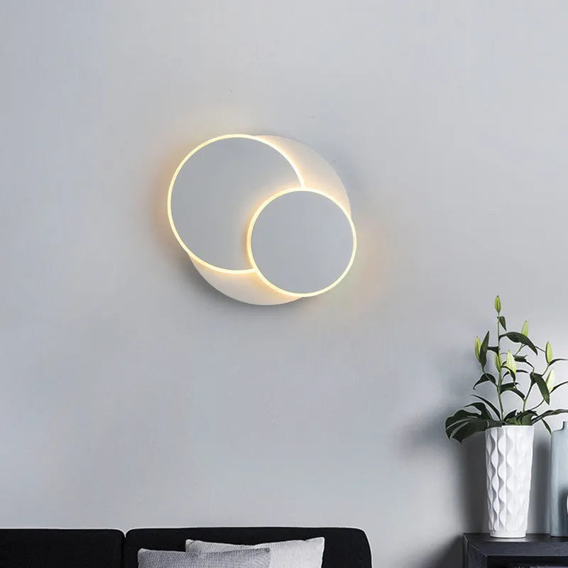 Modern round acrylic wall lamp in black or white on a bedroom wall.