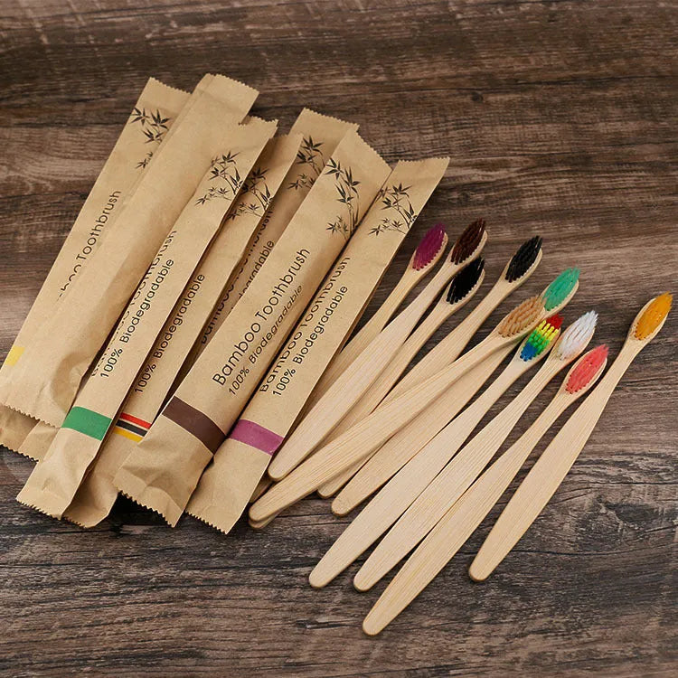 Ten bamboo toothbrushes with coloured handles and charcoal bristles laid out side by side.