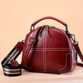 Round portable leather handbag with zipper closure and soft handle in wine red colour