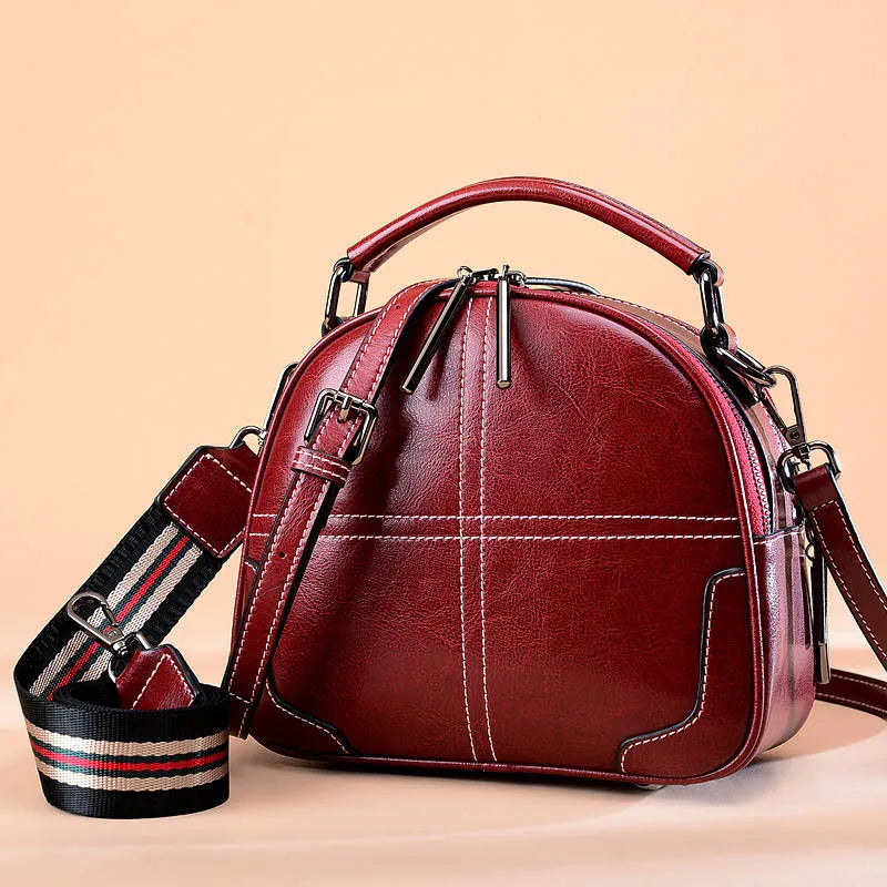 Round portable leather handbag with zipper closure and soft handle in wine red colour