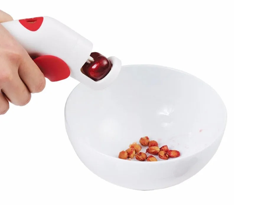 Stainless steel manual cherry kernel remover tool on a kitchen worktop.