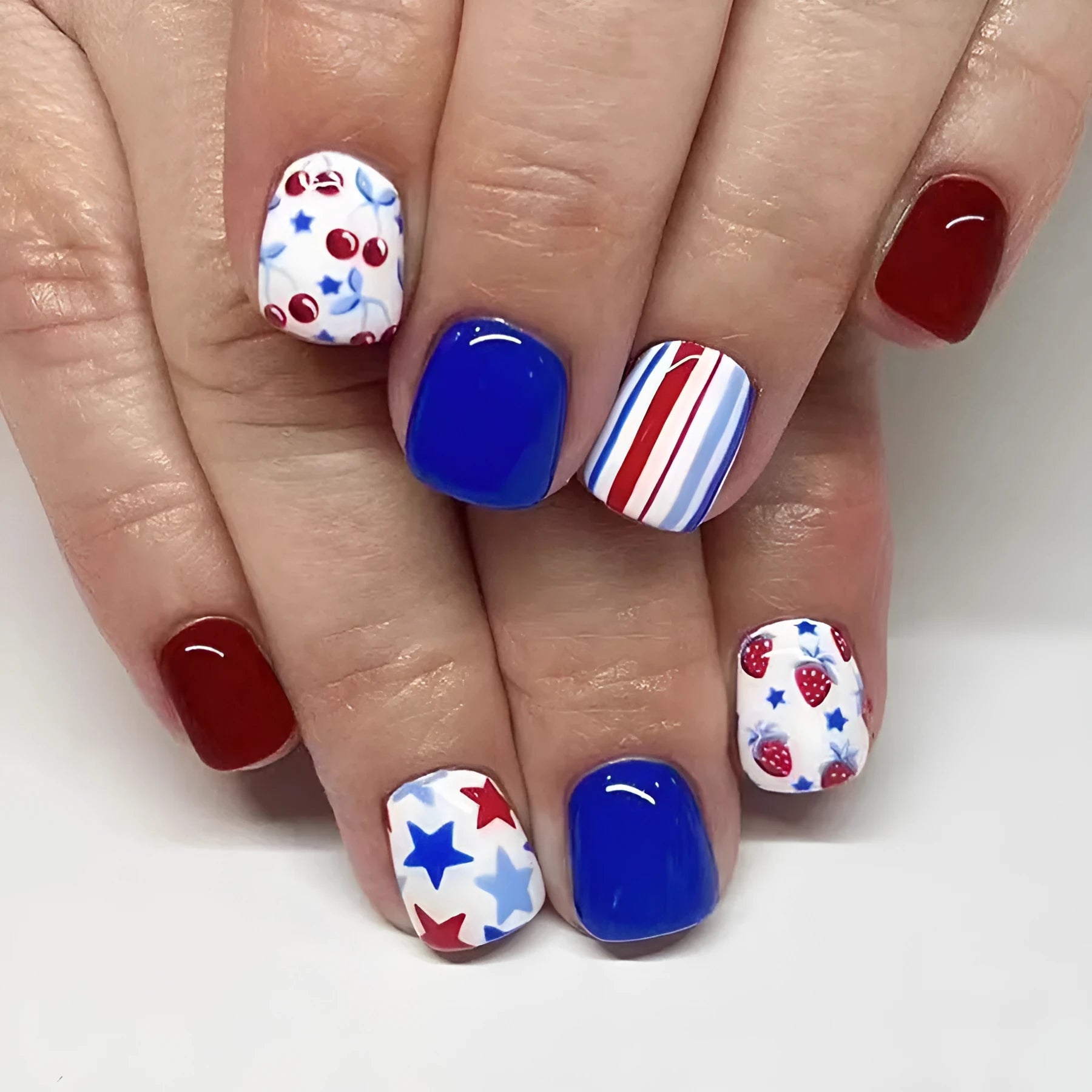 Short glossy red and blue strawberry cherry pattern false nail stickers laid out.