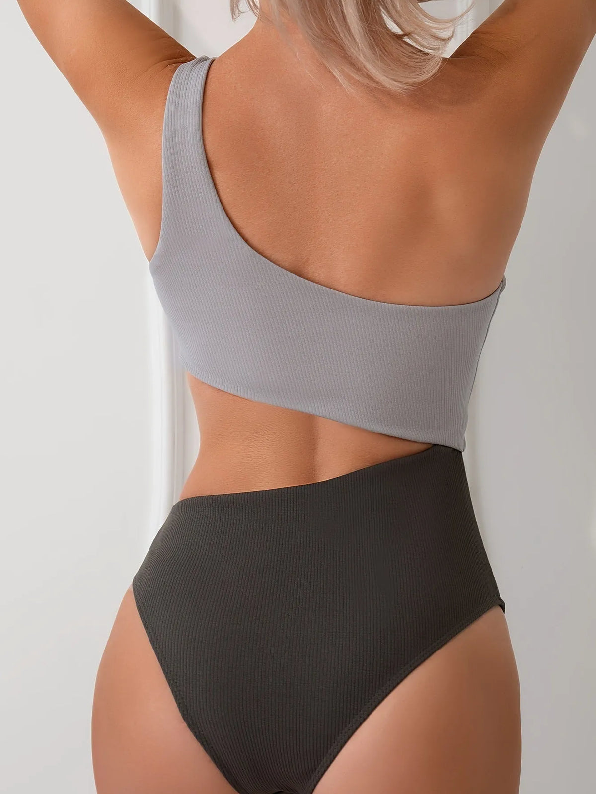 Women's light gray one-shoulder one-piece swimsuit on a neutral background.