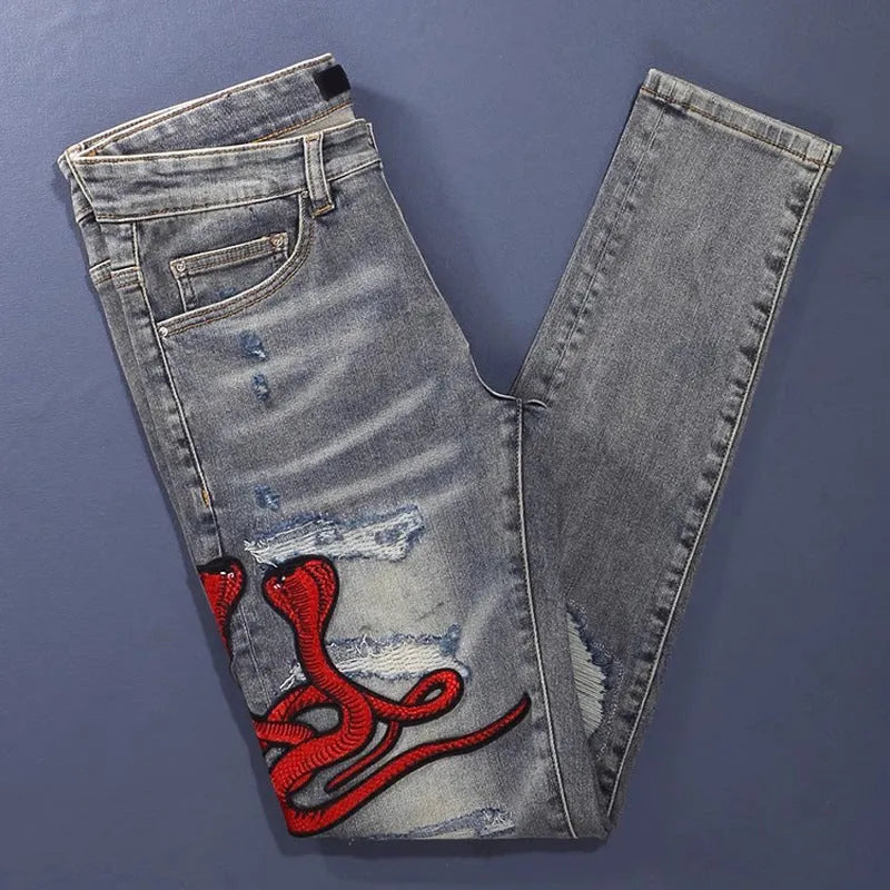 Men's blue slim fit jeans with distressed holes and embroidered patches on faded denim.