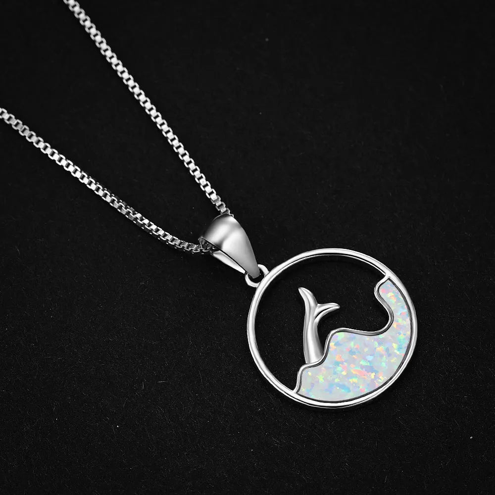 Close-up of a women's geometric fishtail necklace with a round blue opal pendant on a white gold-coloured chain.