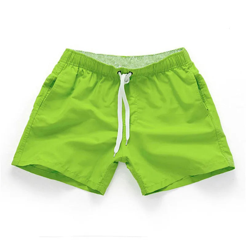 Men's plus size polyester surf shorts on a beach, showing straight leg fit in black and emerald green colours.