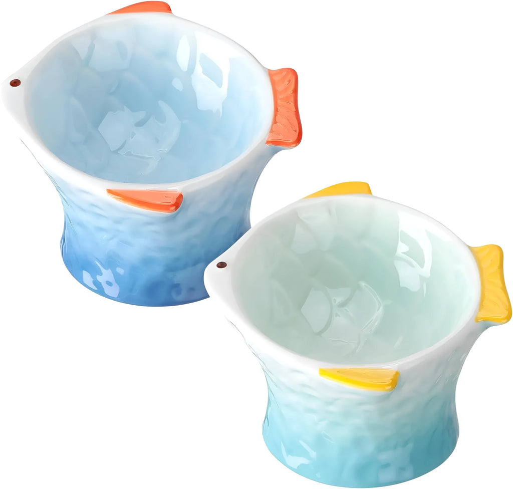 Four coloured fish-shaped ceramic cat bowls with tilted bases on a table.