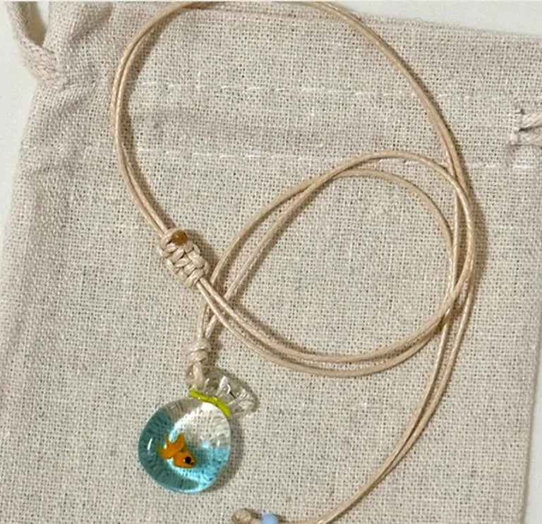 Women's necklace with small coloured glaze fish lucky bag pendant on a braided cotton and linen chain.