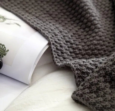 Nordic style beige acrylic throw blanket with fringed knit ball edges on a grey sofa