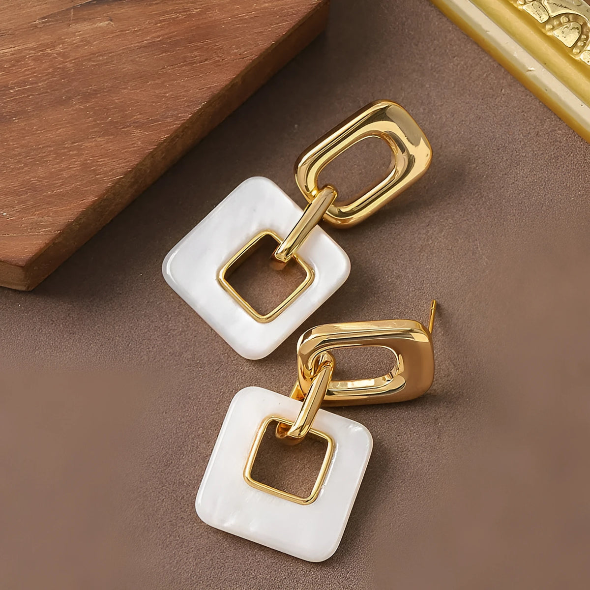 Pair of hollow square earrings with bevelled corners in a metallic finish, shown on a white background.