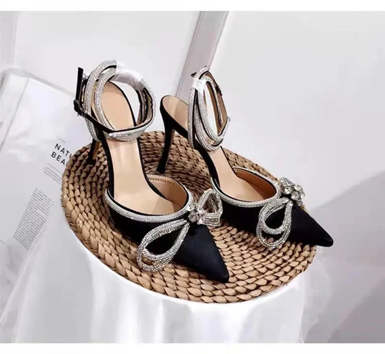 Women's black stiletto heel sandals with a silk bandage strap and buckle fastening on a pointed toe.
