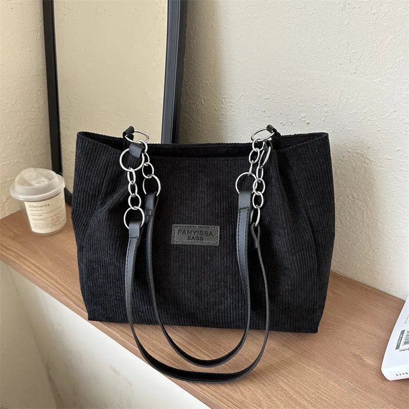 Corduroy one-shoulder tote handbag in black, showing three-dimensional pockets and a large main compartment.