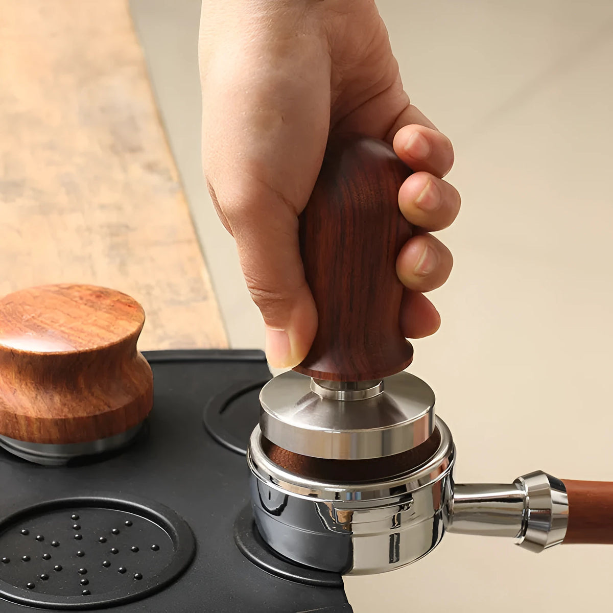 Black manual coffee tamper with stainless steel base and aluminium handle on a coffee station