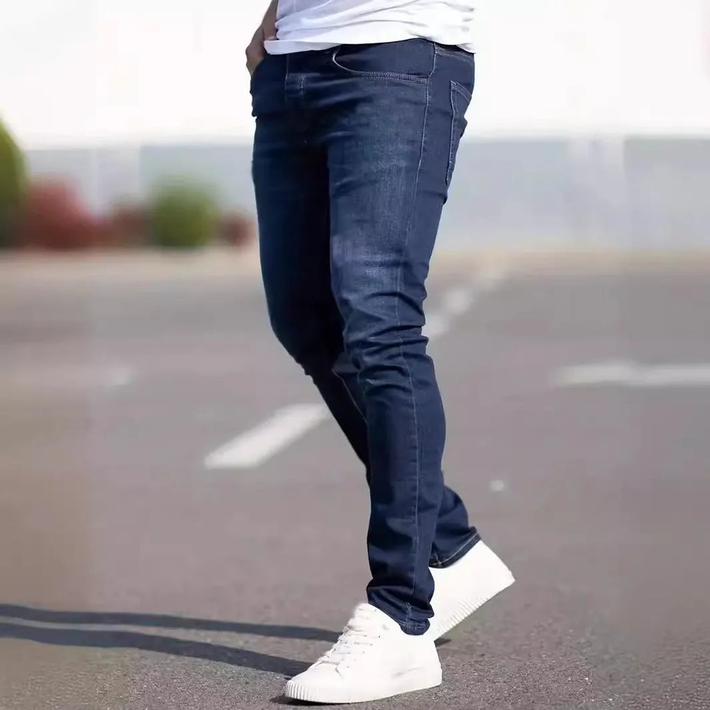 Man wearing dark blue slim-fit skinny jeans with a zipper fly, showcasing the mid-waist and street fashion style.