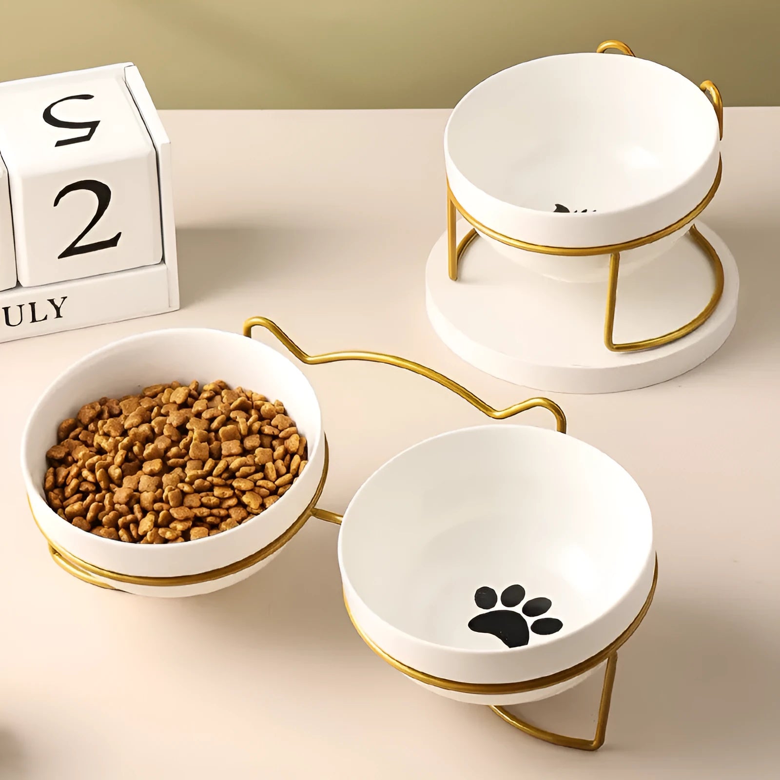 White ceramic cat bowl with cat paw print design on a black iron stand, shown as a pet feeding station.