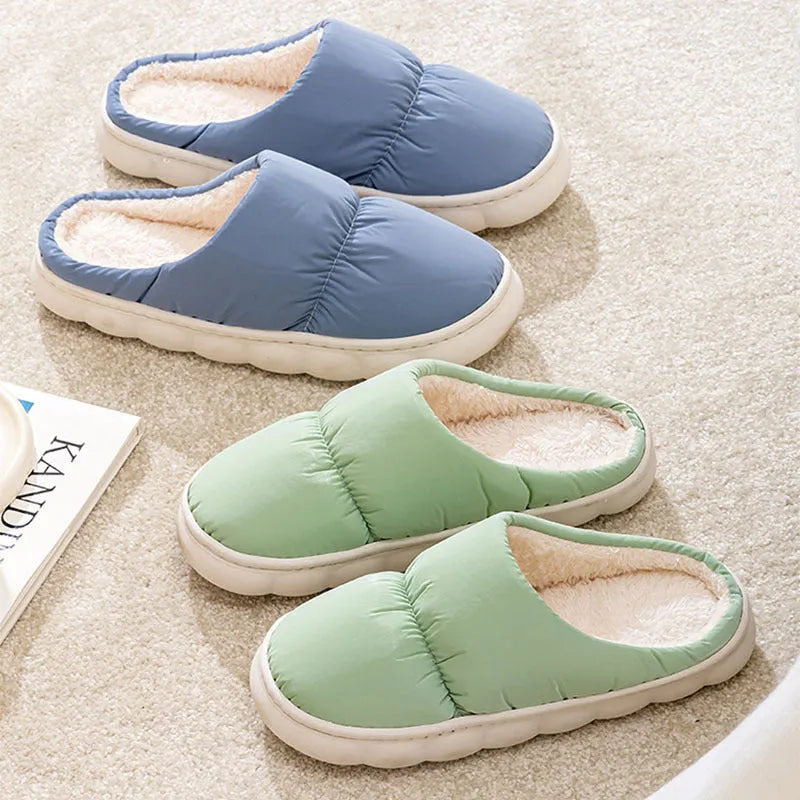 Pair of grey artificial leather slippers with a thick rubber sole and plush lining, shown on a wooden floor.