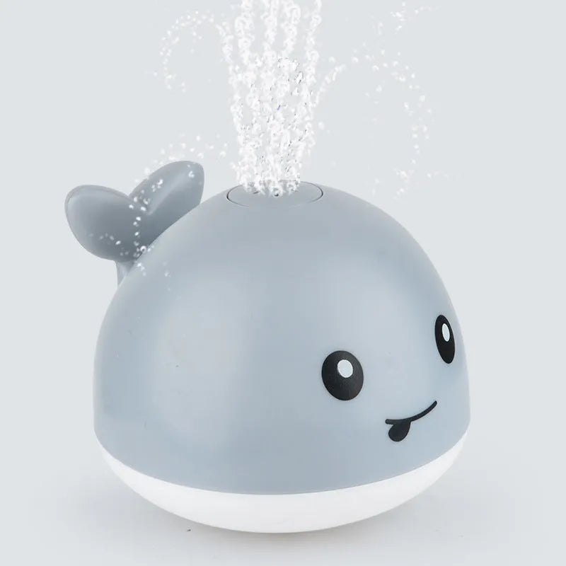 Whale-shaped electric bath toy spraying water with coloured LED lights, shown with base unit on blue background