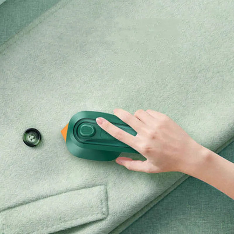 Dark green portable handheld steam iron with ceramic panel, shown next to clothing on a hanger.