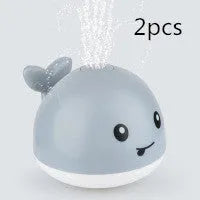 Whale-shaped electric bath toy spraying water with coloured LED lights, shown with base unit on blue background