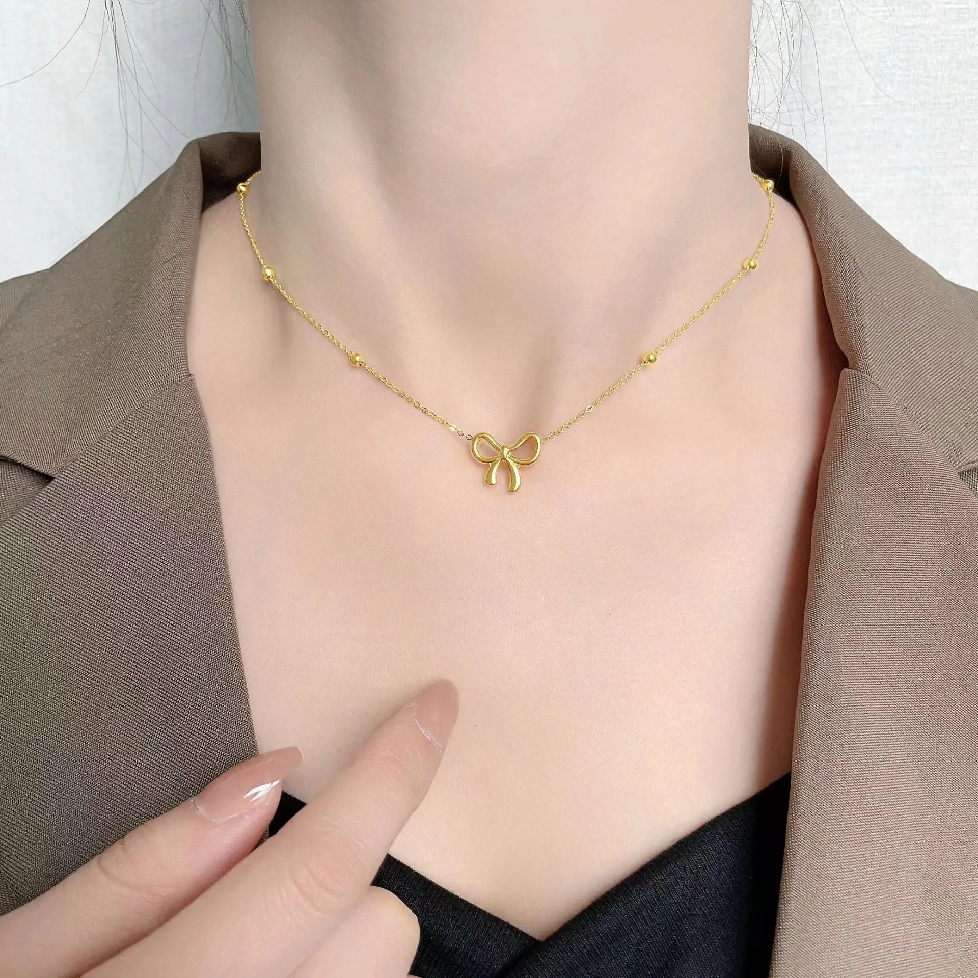 Gold titanium steel bow necklace on a cross chain, adjustable between 41cm and 50cm.