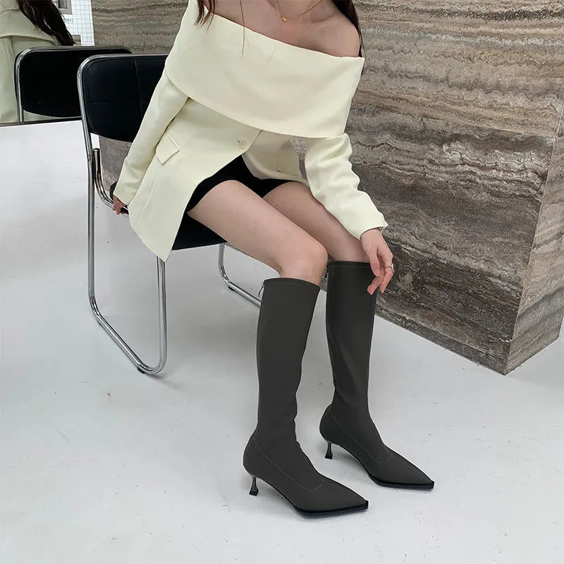 Black pointed toe below knee stiletto heel boots with a back zip, shown on a foot.