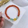 Close-up of a manually crafted red agate bracelet with Lucky Bag and dragon designs on a wrist.