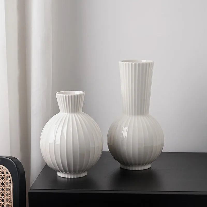 White ceramic ball vase with blue stripes and artificial orchid stems on wooden table.