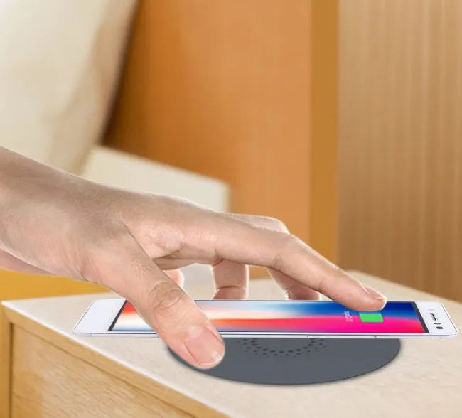 Black 75mm round wireless charging disc for embedding into desks, compatible with iPhone and Samsung phones.