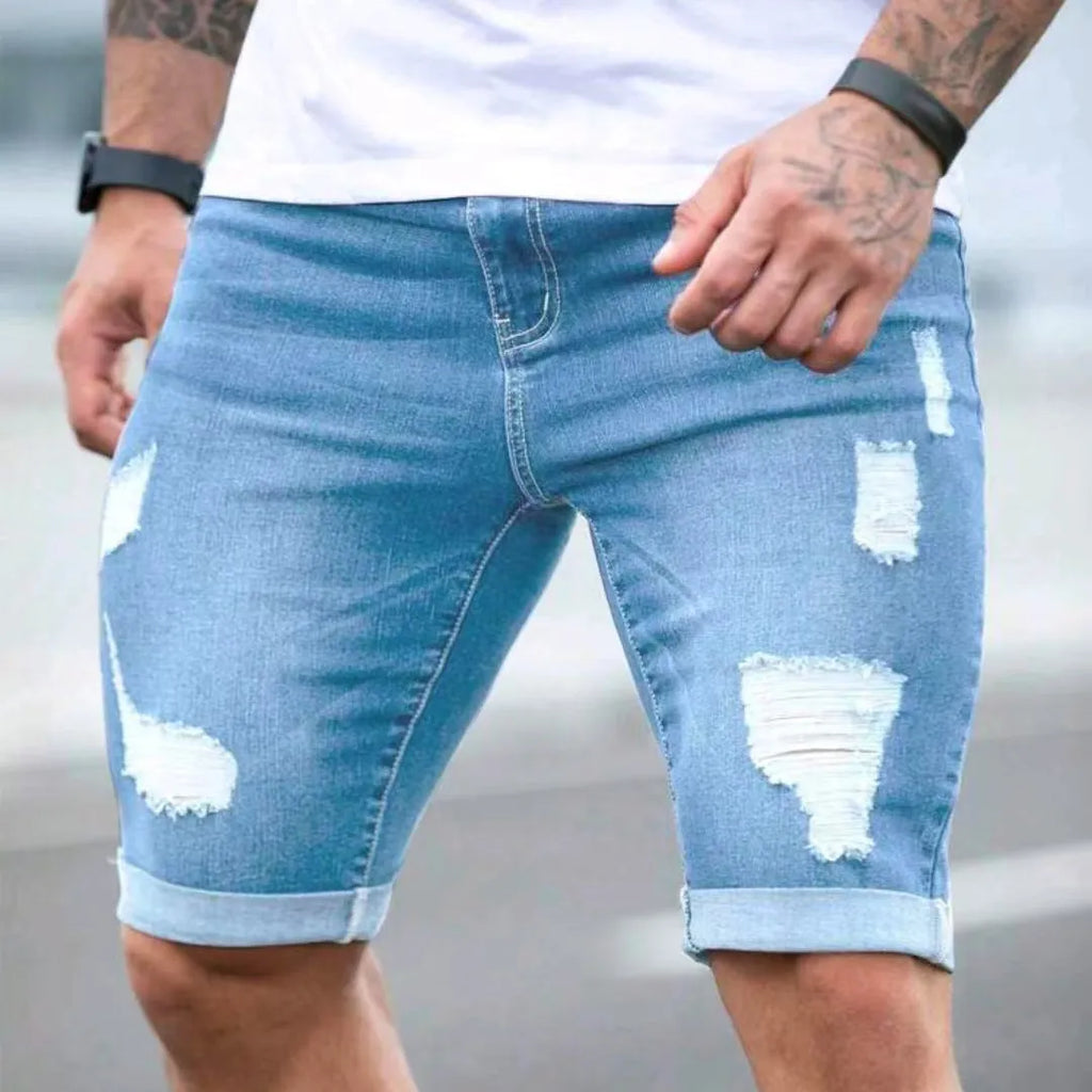 Sky blue men's denim shorts with multi-hole distressing on the legs, showing a low-rise waist and zipper fly.
