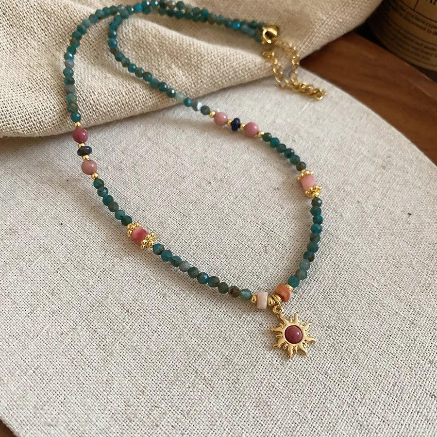 Stone sun pendant freshwater pearl necklace with gold blue pink chain on display.