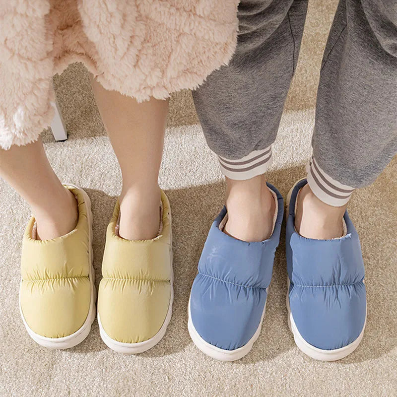 Pair of grey artificial leather slippers with a thick rubber sole and plush lining, shown on a wooden floor.
