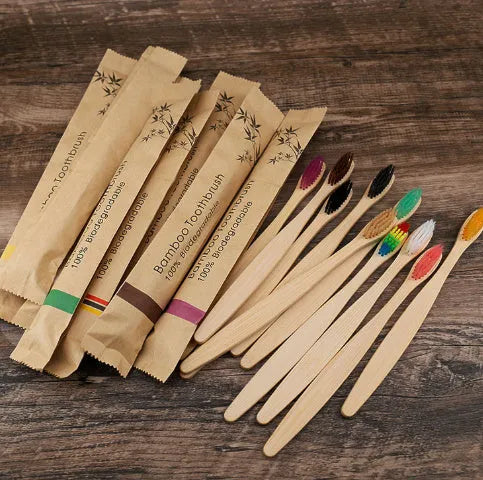 Ten bamboo toothbrushes with coloured handles and charcoal bristles laid out side by side.