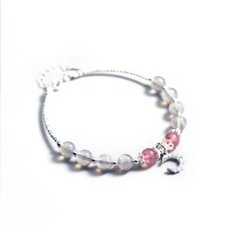 Handmade adjustable moonstone bracelet with a silver crescent moon charm and clear crystal accent on a grey background.